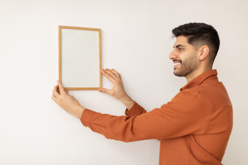 Portrait of cheerfcul man hanging photo frame on the wall