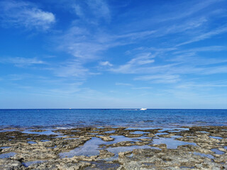 Long-hardened lava, the shore of the Mediterranean Sea against the backdrop of the sea with a white yacht and a blue sky with beautiful clouds.