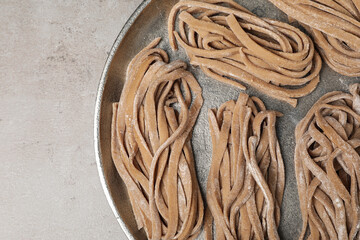 Uncooked homemade soba with tray on light table, top view