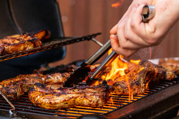 gas grill with grilled meat on fire including grill tongs