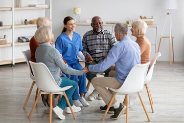 Positive young woman psychologist having group therapy with senior people