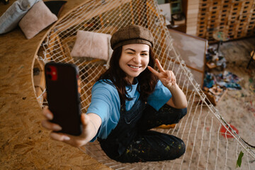 Fototapeta na wymiar Young woman artist gesturing while taking selfie on cellphone
