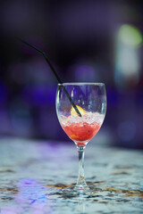 A red alcoholic drink with ice in a glass on the bar counter.