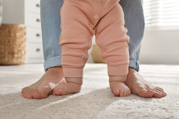 Mother supporting her baby daughter while she learning to walk at home, closeup