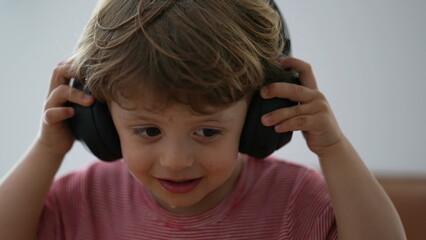 Toddler boy using headphones trying to put but then removing headphones
