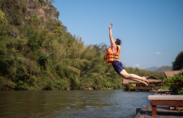 Fototapeta na wymiar A middle-aged woman, about 40, wearing a life jacket, jumped into the river. Fun and acrobatics. The most popular resort activity in Kanchanaburi, Thailand. Jump into the River Kwai. 