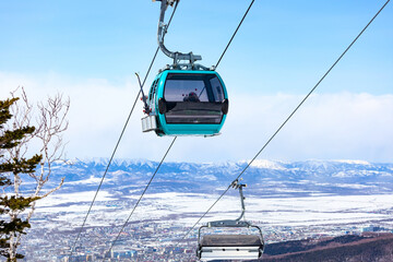 Cable car cabin with the skiers and snowboarders against the snow-covered mountains and city