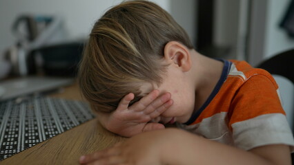 Shy Child covering face with hand little boy sitting at table feeling bore