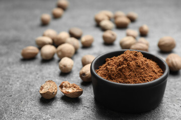 Bowl of nutmeg powder and seeds on grey table, space for text