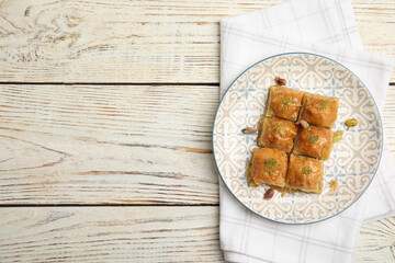 Delicious baklava with pistachio nuts and napkin on white wooden table, top view. Space for text