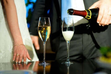 Alcoholic drink champagne is poured into a glass. A man and a woman in the background. A celebration for two.