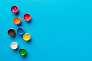 jars with gouache of different colors on Colored background. hobby painting. Top view with empty...