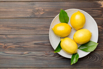 Fresh cutted lemon and whole lemons over round plate on colored background. Food and drink ingredients preparing. healthy eating theme top view vith copy space