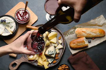 Man pouring red wine from bottle into glass over black table with snacks, top view