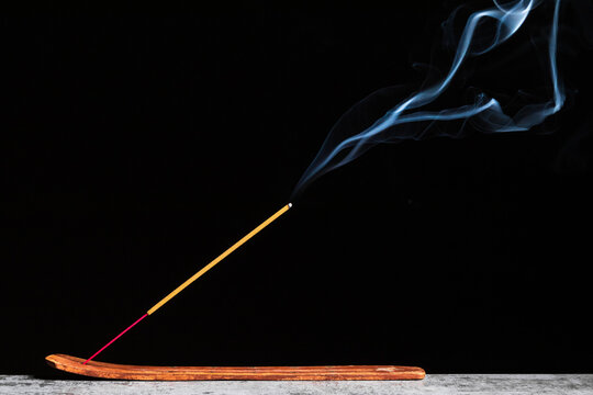 Burning stick of incense stands on a wooden stand isolated on a black background
