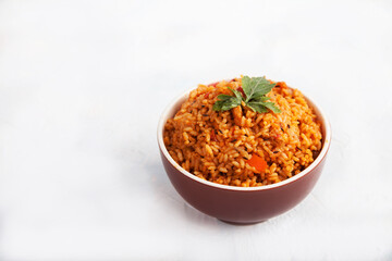 Jollof rice with parsley in a ceramic cup on a white background. National cuisine of Africa. Copy spaes.