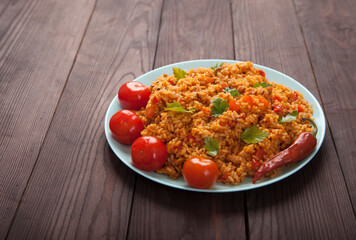 Jollof rice, tomatoes and hot peppers on a blue plate on a wooden background. National cuisine of Africa.