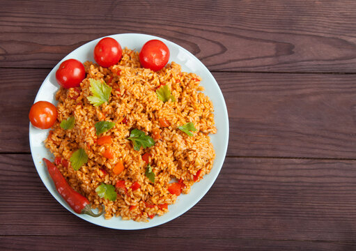 Jollof rice, tomatoes and hot peppers on a blue plate on a wooden background. National cuisine of Africa.