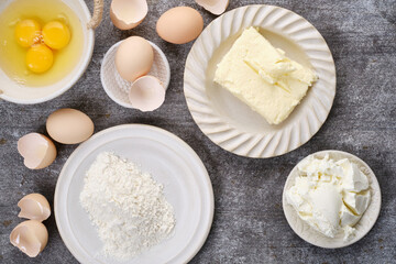 Muffin, baking ingredients: Butter, flour, whole eggs, broken eggs, yolk on a bowl cocoa in plates on the table