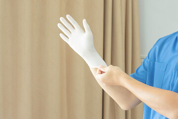 A doctor wearing a blue uniform puts on rubber gloves. in the clinic before treating a patient.