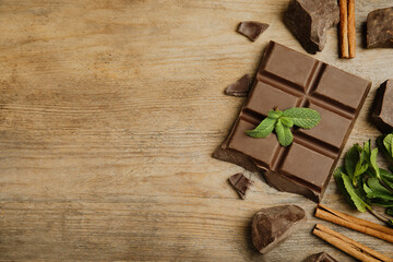 Tasty chocolate pieces, cinnamon sticks and mint on wooden table, flat lay. Space for text