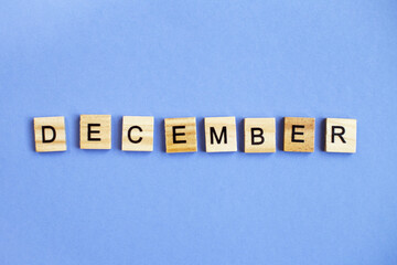 inscription December made by wooden cubes on a veri peri purple background.