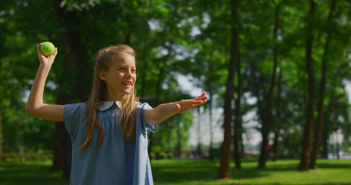Smiling girl throw ball on green meadow closeup. Happy kid play catch in park.