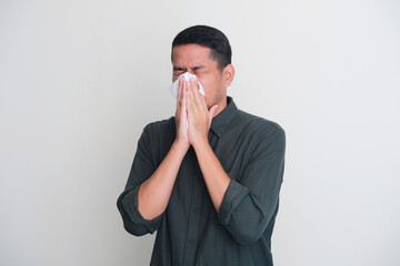 Adult Asian man cover his nose and mouth with tissue when sneezing