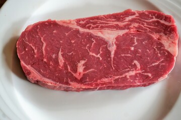 Rohes Rumpsteak auf weißem Teller auf Naturholztisch