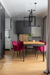 Elegant dining room interior design with velvet chairs, design wooden table, lamps and beautiful personal accessories. Open space. Concrete walls. Modern home decor. Template.