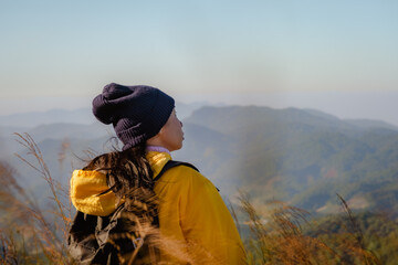 Rear view of a woman in a yellow jacket standing on top of a mountain at sunrise and looking up while enjoying a quiet day in nature breathing in the fresh air.