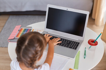 Indoor shot of dark haired female child with braids typing on keyboard, doing her school tasks,...