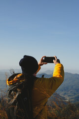 Woman hiking with backpack using smartphone to record beautiful mountain memories and experiences. Happy and excited young woman in outdoor adventure