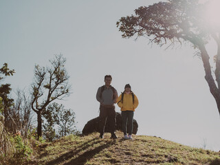 A couple of male and female tourists stand on top of the mountain raising their hands in victory. Happy couple with backpacks hiking in forest in autumn.