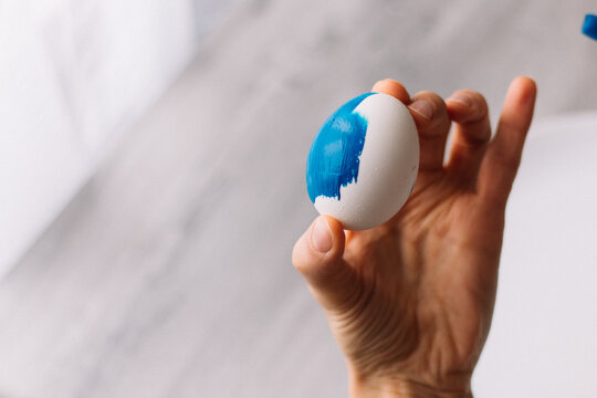 Close-up. Female hands paint Easter egg in a modern minimalist style with blue paint. Traditional symbols. Preparation for Easter.