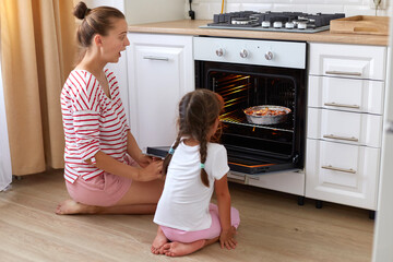 Indoor shot of surprised amazed woman wearing striped shirt and child in white t shirt sitting on...