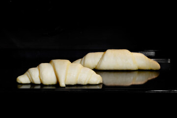 Two uncooked croissants on tray in electric oven - close up view. French cuisine, homemade bakery, breakfast, food, cooking, pastry, semi-finished products and raw concept