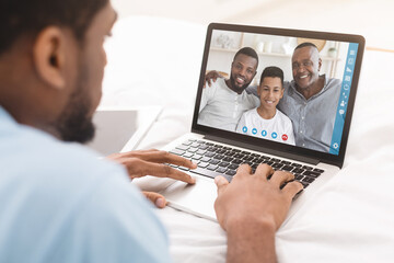 Black guy having video call with family, lying on bed with laptop, communicating to his nears remotely from home