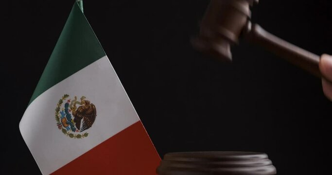 Wooden gavel striking on sound block near the Mexico flag. Black background. Judge Pronouncing Sentence striking Gavel.