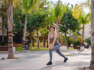 Fototapeta na wymiar outdoor sports, workout and wellness concept. asian young strong, confident woman in sportive clothes in green park warming up before jogging outdoors, leg stretching before running.