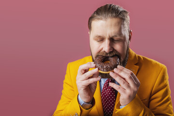 Caucasian mature man in stylish yellow jacket eating delicious chocolate donut with closed eyes...