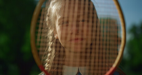 Joyful little kid making funny face with badminton racket. Girl pressing nose