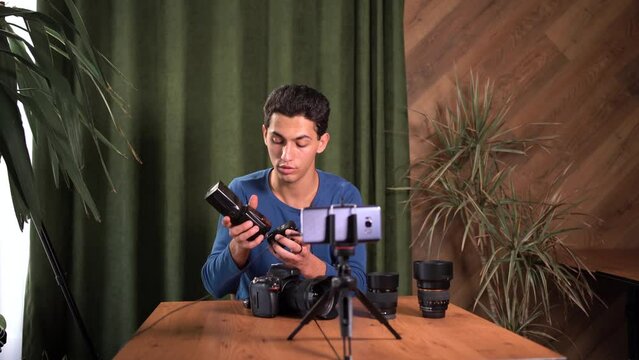 training for beginner photographers, online courses. A Muslim man records a video review of photographic equipment using an application on a smartphone. Radio synchronizers their purpose