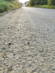 A rough concrete road with small and large gravel heading straight ahead in the evening, rough road.