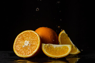 Water pours on oranges on a black background. Spray of water on cut oranges. Refreshing fruit