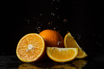 Fototapeta na wymiar Water pours on oranges on a black background. Spray of water on cut oranges. Refreshing fruit