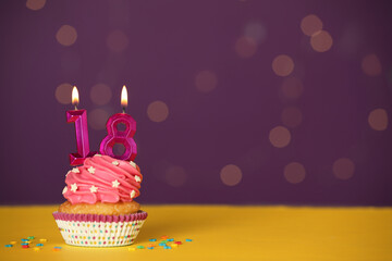 Coming of age party - 18th birthday. Delicious cupcake with number shaped candles on yellow table...