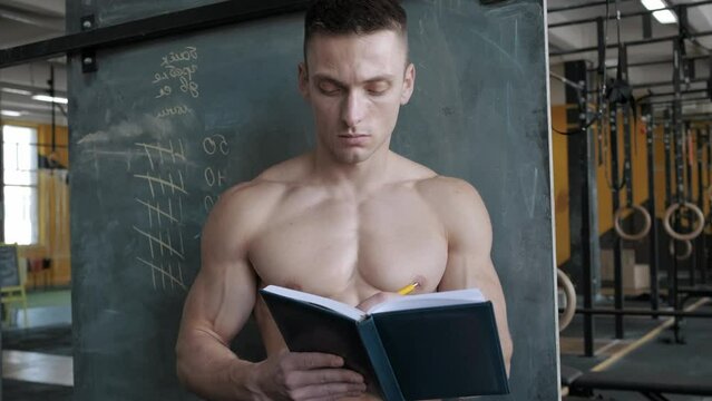 Muscular athletic man writes results in a notebook in the gym. Sport, weight lifting and health care concept
