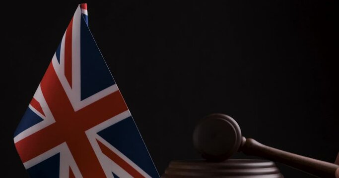 Referees hammer hits the shock block near the Great Britain flag, black background. Wooden Mallet next to Great Britain flag.