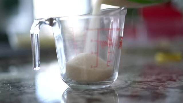 Pouring cane sugar into glass measuring cup for recipe for certain quantity